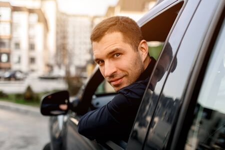 A well-looking man looks from his car and looks back. The driver is in a residential area of the cityの写真素材