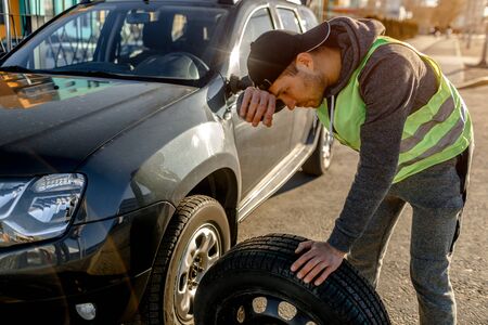 Transportation, traveling concept. Worker changes a broken wheel of a car. The driver should replace the old wheel with a spare. Man changing wheel after a car breakdownの写真素材