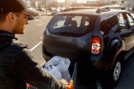 buying food in a supermarket. Shopping A young man buys food for a week in a large shopping center in the countryside. Folds bags of vegetables, fruits, meat and dairy products in a car park.の写真素材