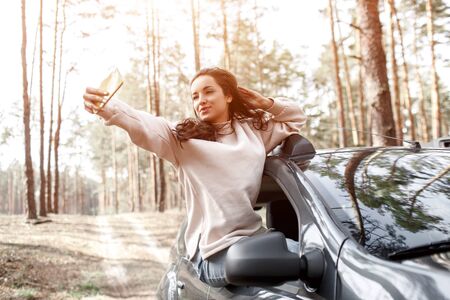 Happy young woman climbed out of a car window. Traveling by car in the forest. Country trip....