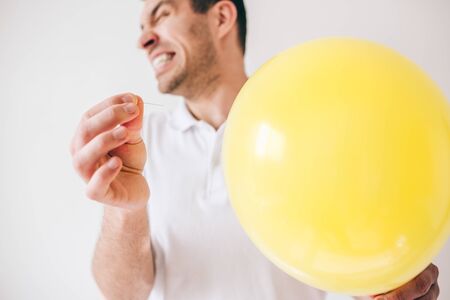 Young man isolated over white background. Guy pierce a balloon with needle. Afraid of sound. Cut view and close up. Defocused guy on picture.の写真素材