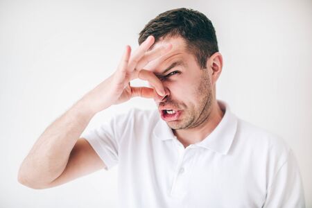 Young man isolated over white background. Guy covers his nose with fingers due to a bad smell. Look...