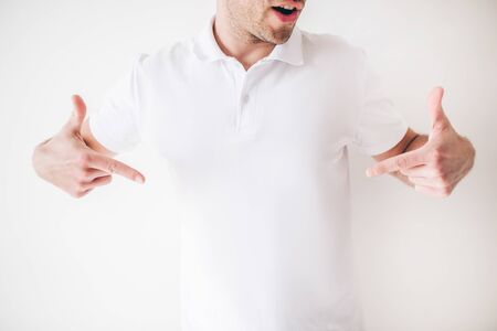 Young man isolated over white background. Cut view of cool confident male person point down with both hands fingers. Guy in white shirt in studio alone.の写真素材