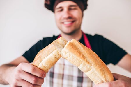Young man isolated over background. Baker isolated on holding and crunching traditional bread french...