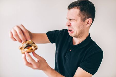 Young man isolated over white background. Guy look inside burger with disgussion. Bad smell and untasty fast food.