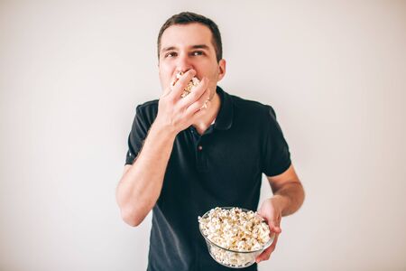 Young man isolated over white background. Guy eating popcorn from bowl. Tasty delisious snack. Glutton man divour meal.の写真素材