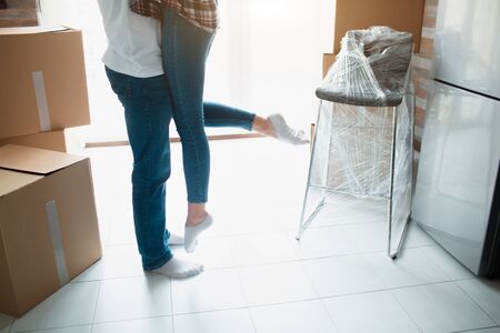 Young couple first time home owners celebrate moving day concept, man husband lifting holding wife standing near boxes in new own house apartment, relocation and family mortgage.の写真素材