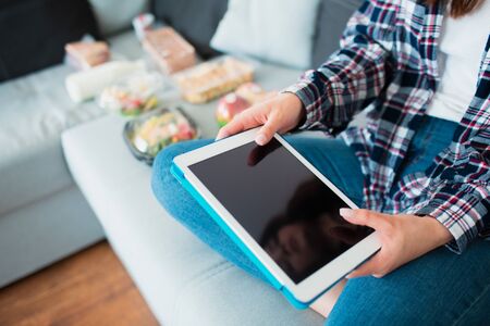 Food delivery concept. A young woman orders food using a tablet at home.