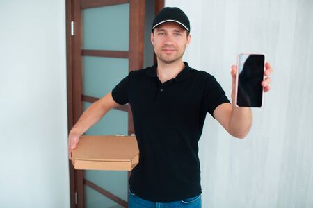 Food delivery concept. Pizza Delivery Man Shows App On Smartphone For Deliveryの写真素材