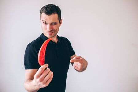Young man isolated over background. Guy hold ripe hot pepper in hand and show it on camera. Ready for cooking.の写真素材