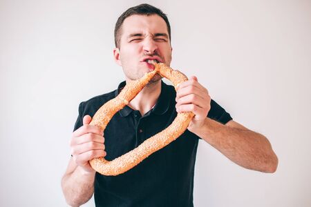 Young man isolated over background. Picture of guy holding big round bun and biting it with pleasure. Stand alone in studio and posing.の写真素材
