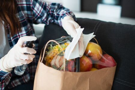 Food delivery concept. A young girl in gloves is processing antiseptic products. She came from the grocery store and brought a lot of food in bags.の写真素材