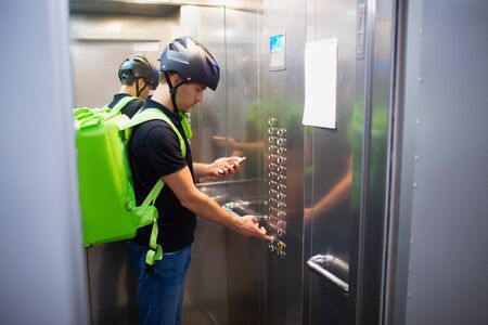 Food delivery concept. The food delivery man goes up in the elevator to find the apartment that placed the order.の写真素材