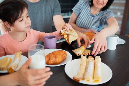 Close-up. Happy breakfast of a large family in the kitchen. Siblings, parents and children, mother and grandmother. Father and daughter. Everyone is eating in the morning and chatting and having fun.の写真素材