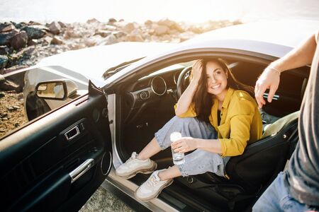 Romantic couple is standing near a Muscle car on the beach. The handsome bearded man and an...