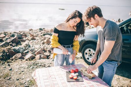 Travel, tourism - Man and woman drink champagne near the water at a folding portable table. Picnic near the water. Couple going on Adventure. Car travel concept.の写真素材