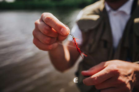 Young fisherman fishing on lake or river. Close up and cut view of artificial plastic lure in guy's hands. Fisherman adjusting his equipment before fishing processの写真素材