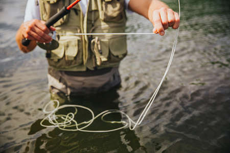 Young fisherman fishing on lake or river. Cut view of guy standing alone in water and holding some fishing line in hands. Preparing equipment for fishing timeの写真素材