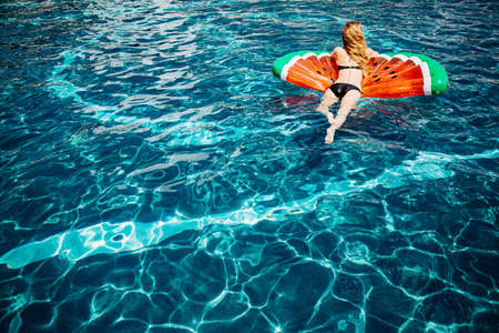 Young hot woman resting at swim-pool. Back view picture of relaxed slim woman in black swimsuit...