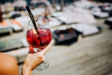 Cut view of girls hands holding red cold cocktail with ice cubes inside.の写真素材