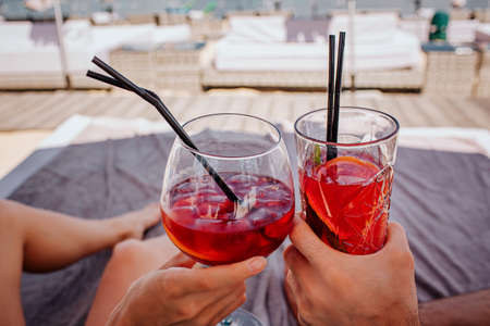 Young hot couple resting at swimpool. Picture of two red cold cocktails with ice cubes cheering....