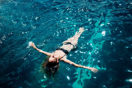 Young hot woman resting alone. Picture of calm relaxed girl in water swimming. Looking up in sky and taking sunbathing. Enjoy summer vacation alone.の写真素材