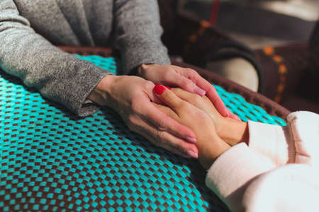 Mature mother and her young daughter sit together in cafe or restaurant. Supportive hands holding together. Red manicure. Helping hand. Together. Mother and daughter.の写真素材