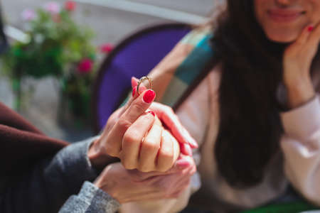 Mature mother and her young daughter sit together in cafe or restaurant. Cut view of girl holding engagement ring with fingers and rejoice. Mother support share her happiness. Getting married soon.の写真素材