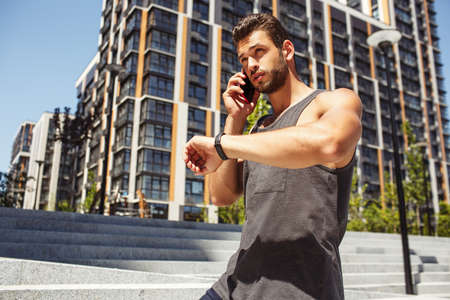 Young man exercising outside. Stand alone in middle of urban street and talking on phone. Looking at...