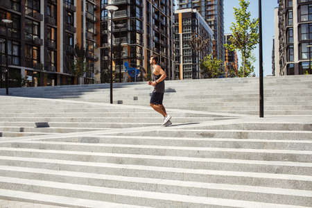 Young man exercising outside. Picture of guy running or jogging alone outside near steps. Urban city...