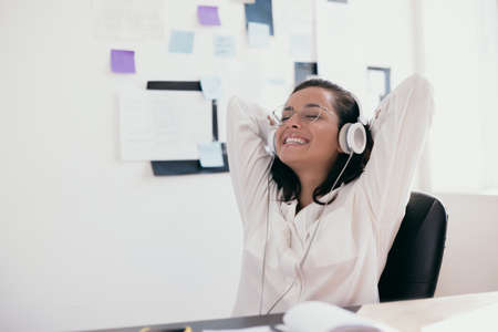 Intelligent young woman with arms on head relaxes listening to music. Happy female office or...