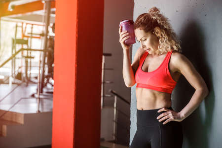 A woman is holding a bottle of water near her head.の写真素材