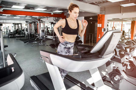 A young girl is running on a treadmill in a gym. She is looking forward