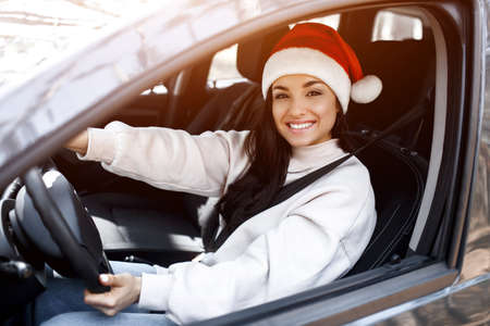 Happy New Year and Merry Christmas A woman is sitting in a car, she is wearing a red santaclaus hat and smilingの写真素材