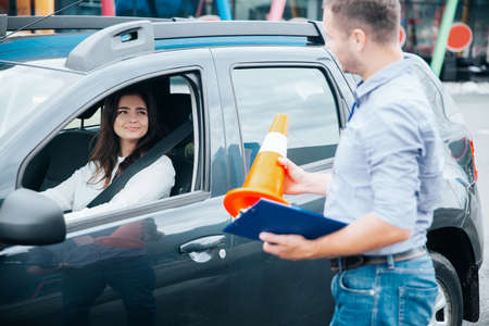 Male instructor in jeans and gray shirt shows road cone to his female student. Attractive female...