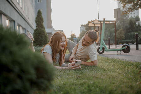 Charming girl and an attractive guy are lying on the grass with smart phone. Couple is using eco transportの写真素材
