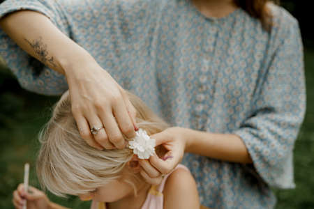Young mother is pinning hair of her child in the garden. Family time.の写真素材