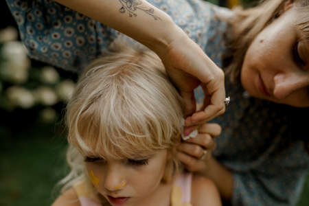 Young mother is pinning hair of her child in the garden. Family time.の写真素材