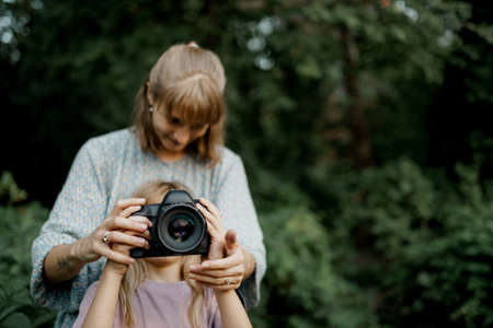 Mother is teaching her young daughter to use a camera outside in spring natureの写真素材