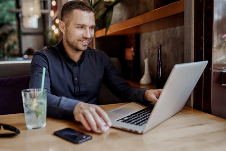 Young businessman is having online meeting on laptop in restaurant. Remote work.の写真素材