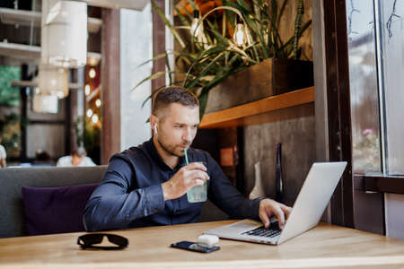 Young businessman is working on laptop in restaurant in earpods. Remote work.の写真素材