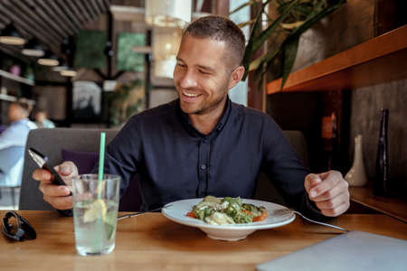 Smiling businessman is using his phone while having lunch in restaurantの写真素材