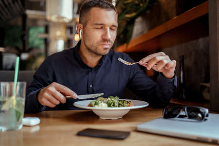 young businessman in EarPods is enjoying his lunch in restaurant. listening to music.