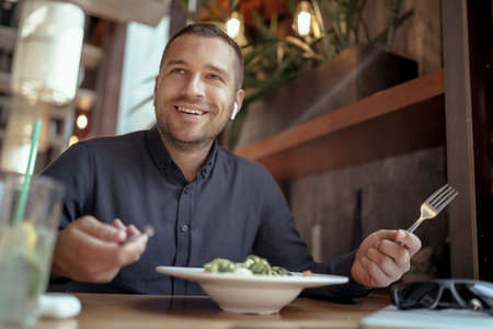 young businessman in EarPods is having lunch in restaurant. listening to music.の写真素材