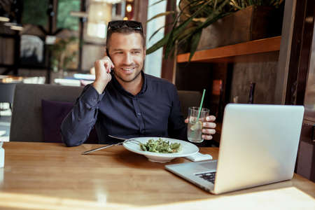 businessman is having lunch while talking on phone in restaurant. remote work.の写真素材