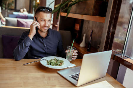 businessman is having lunch while talking on phone in restaurant. remote work.の写真素材