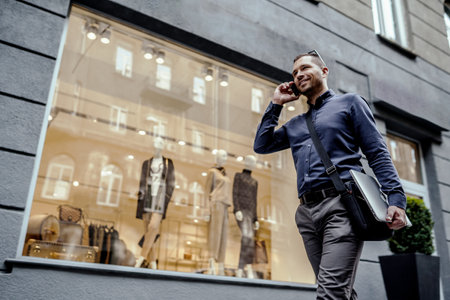 Young businessman holding his laptop while talking on phone. Walking on the street.の写真素材