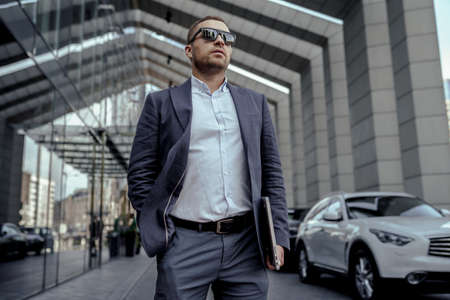 Young businessman in sunglasses holding his laptop. Walking on the street.の写真素材