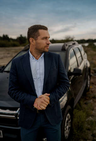 Portrait of businessman with black classic car wearing suit. Man is standing near his car outdoors.の写真素材