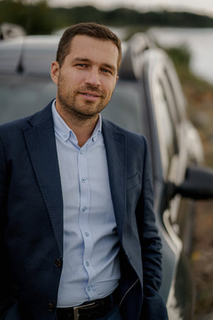 Portrait of businessman with black classic car wearing black suit. Man is standing near his car outdoors.の写真素材